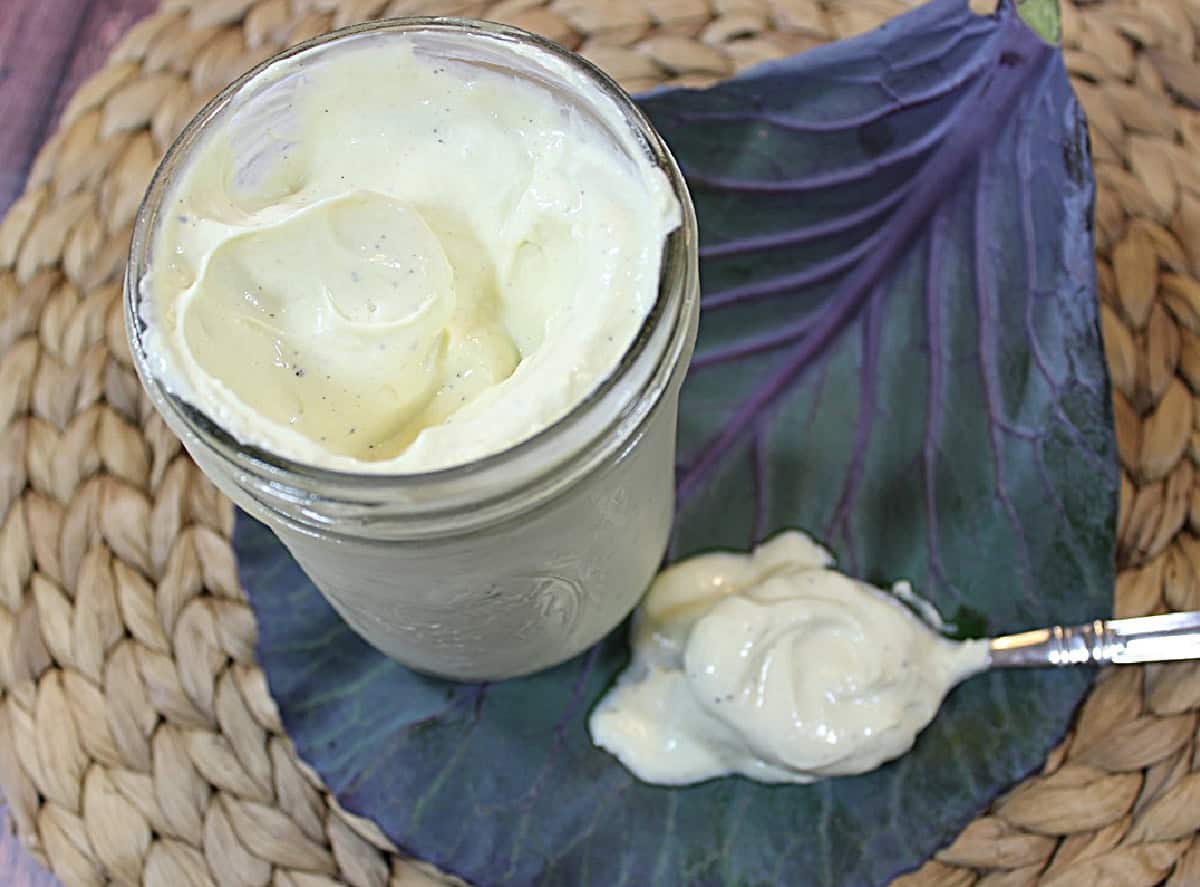 A mason jar and a spoonful of avocado oil mayonnaise on a woven placemat.
