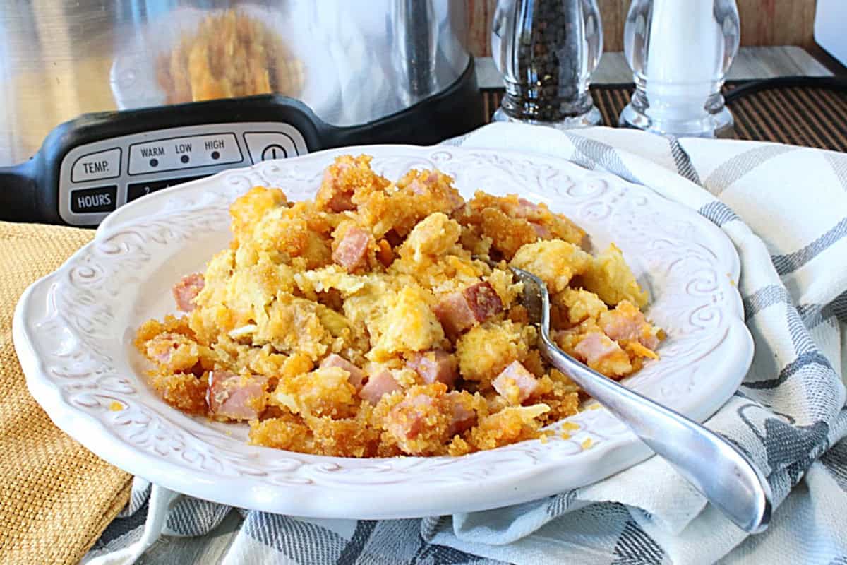 A bowl, spoon, and a serving of slow cooker ham and cheese strata.