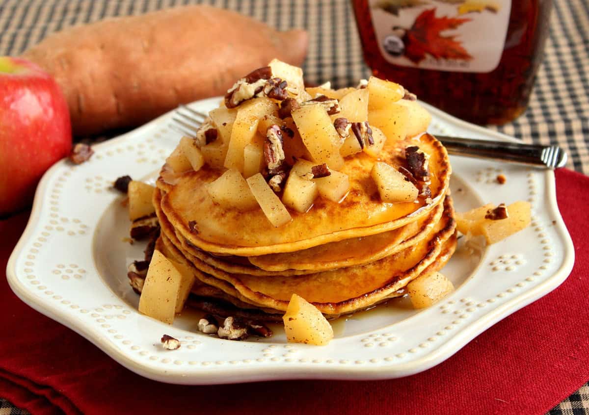 Sweet Potato Pancakes with Apples and Pecans A pretty white plate with a serving of sweet potato pancakes along with apples and pecans on top.
