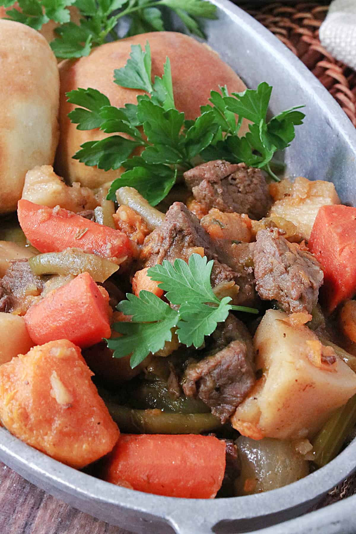 Close up image of beef stew with carrots, onions, green beans and sprigs of parsley.