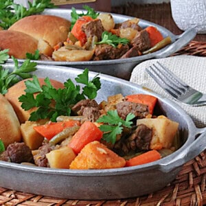Two comforting looking servings of apple cider beef stew in oval, sliver serving dishes.