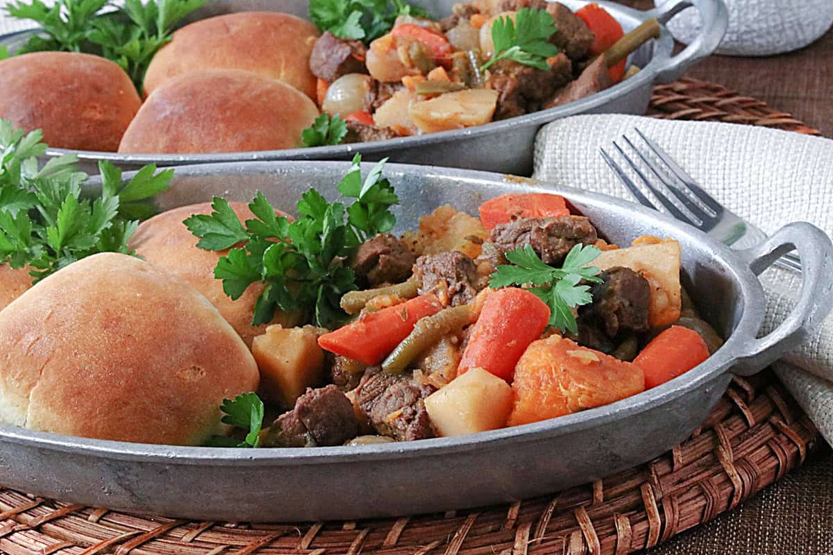 Two oval dishes filled with servings of apple cider beef stew with carrots and parsnips.