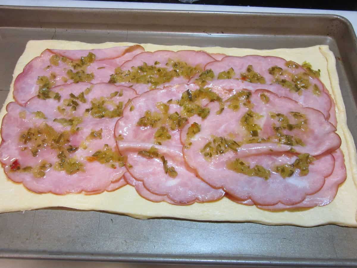 Slices of ham along with some pickle relish spread out on top of crescent roll dough.