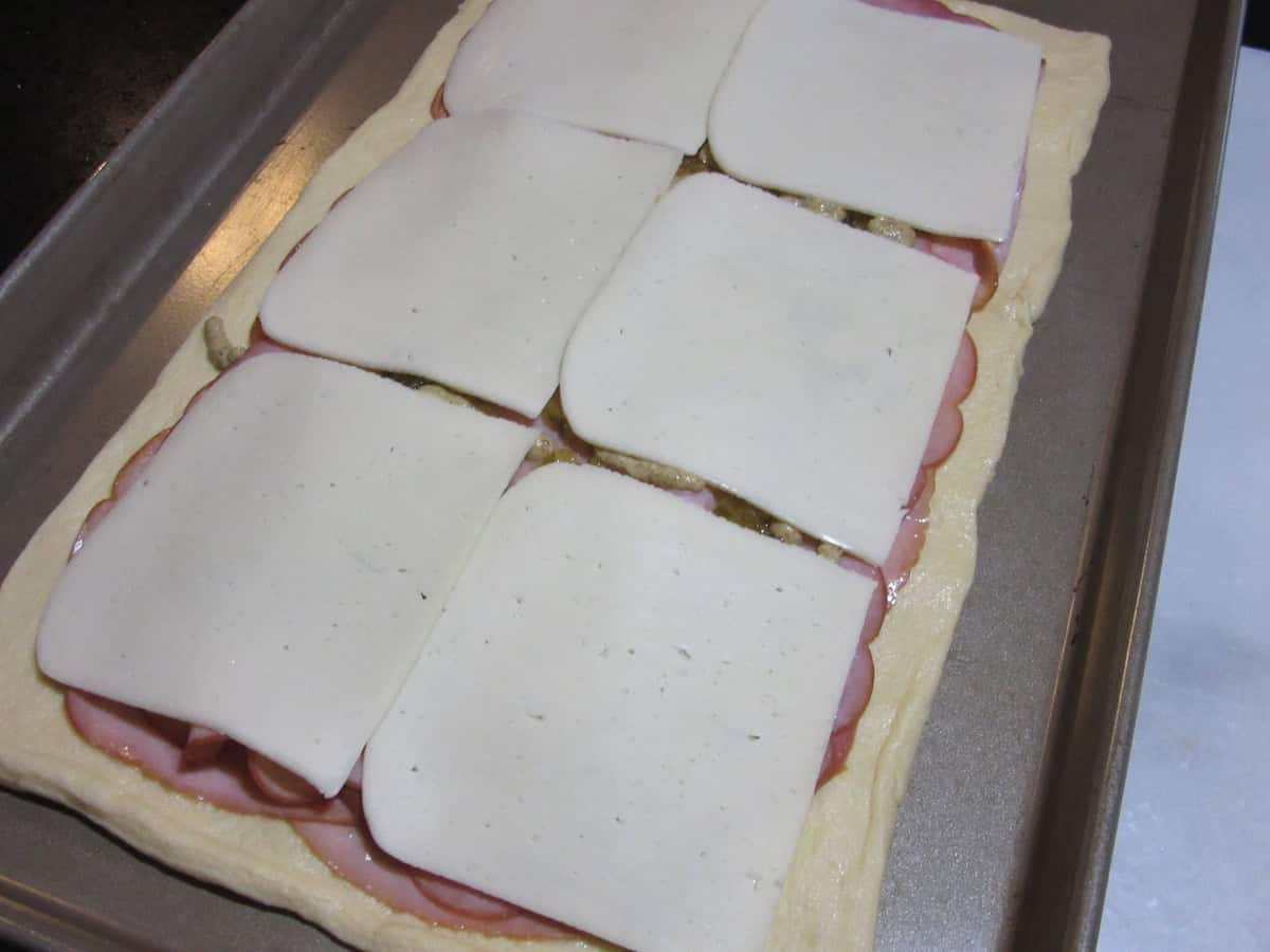 Slices of cheese layered out on top of crescent roll dough.