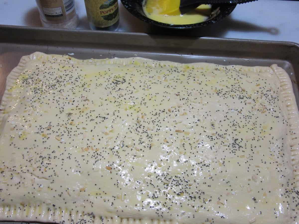 Poppy seeds sprinkled on top of an unbaked crescent roll dough sheet.