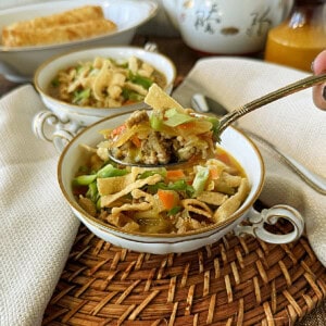 Two bowls of egg roll soup on a woven wicker placemat with a dish of egg rolls in the background.