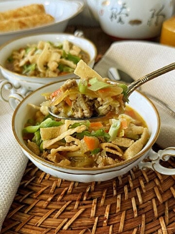 Two bowls of egg roll soup on a woven wicker placemat with a dish of egg rolls in the background.