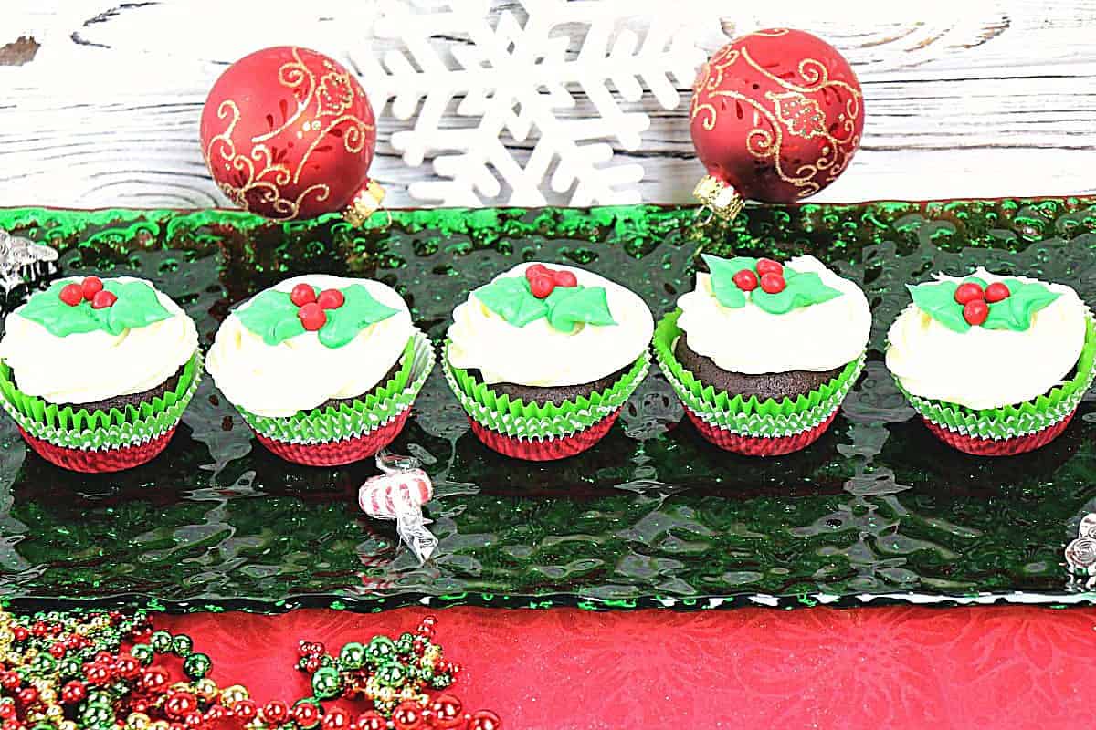 A green glass rectangle plate with a row of holly berry chocolate cupcakes on top.