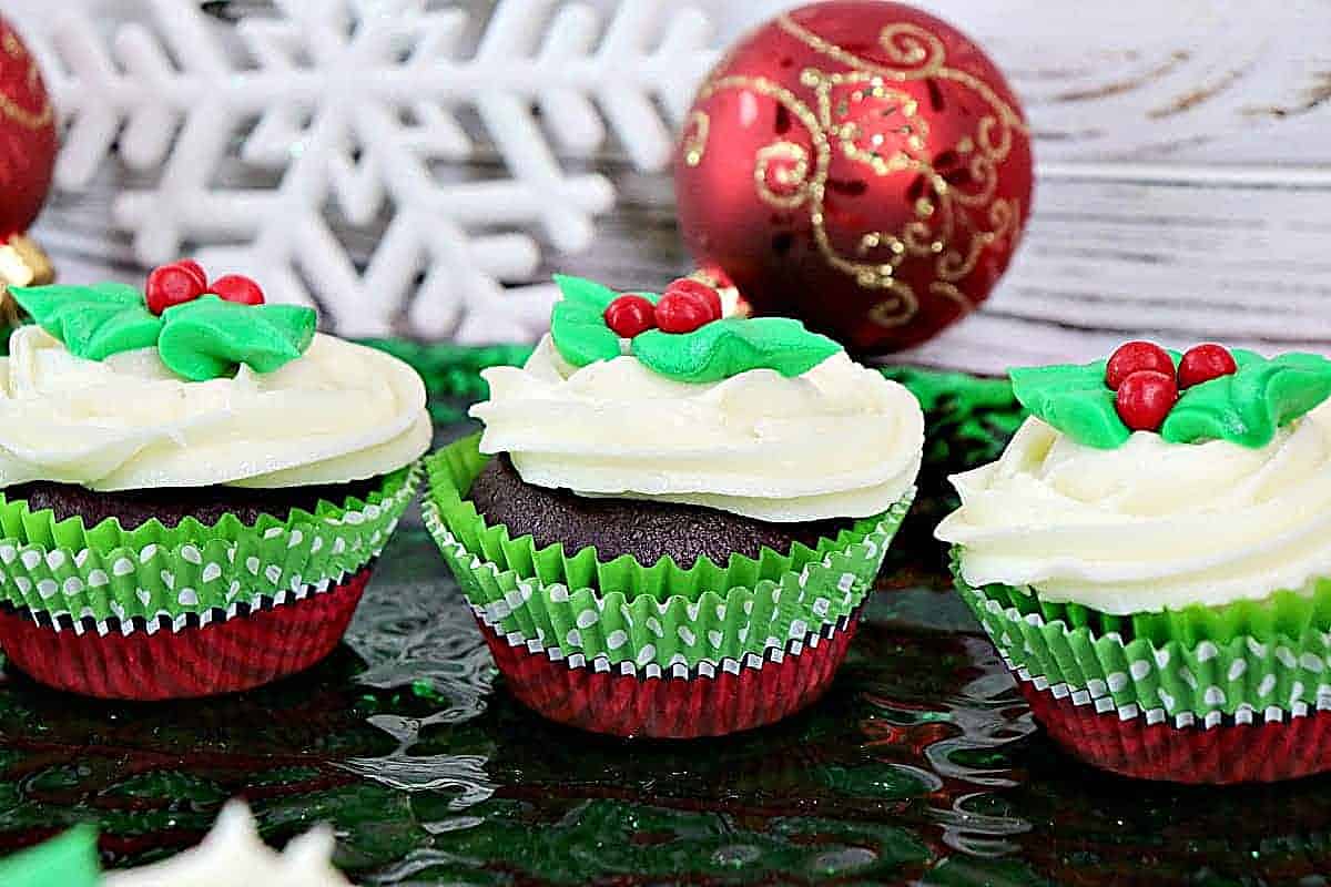 Three chocolate holly berry cupcakes in a row with cute and festive frosting and cupcake liners.