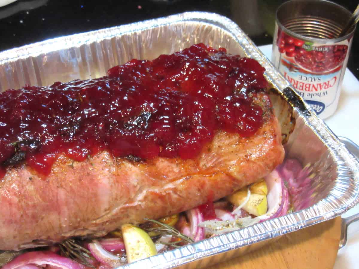 Cranberry relish topped on a roasted pork roast in a roasting pan.