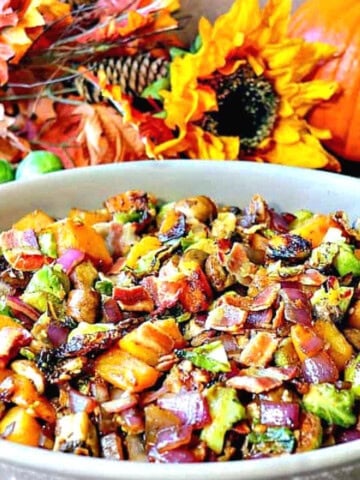 A casserole dish filled with colorful sauteed autumn vegetables with sunflowers in the background.