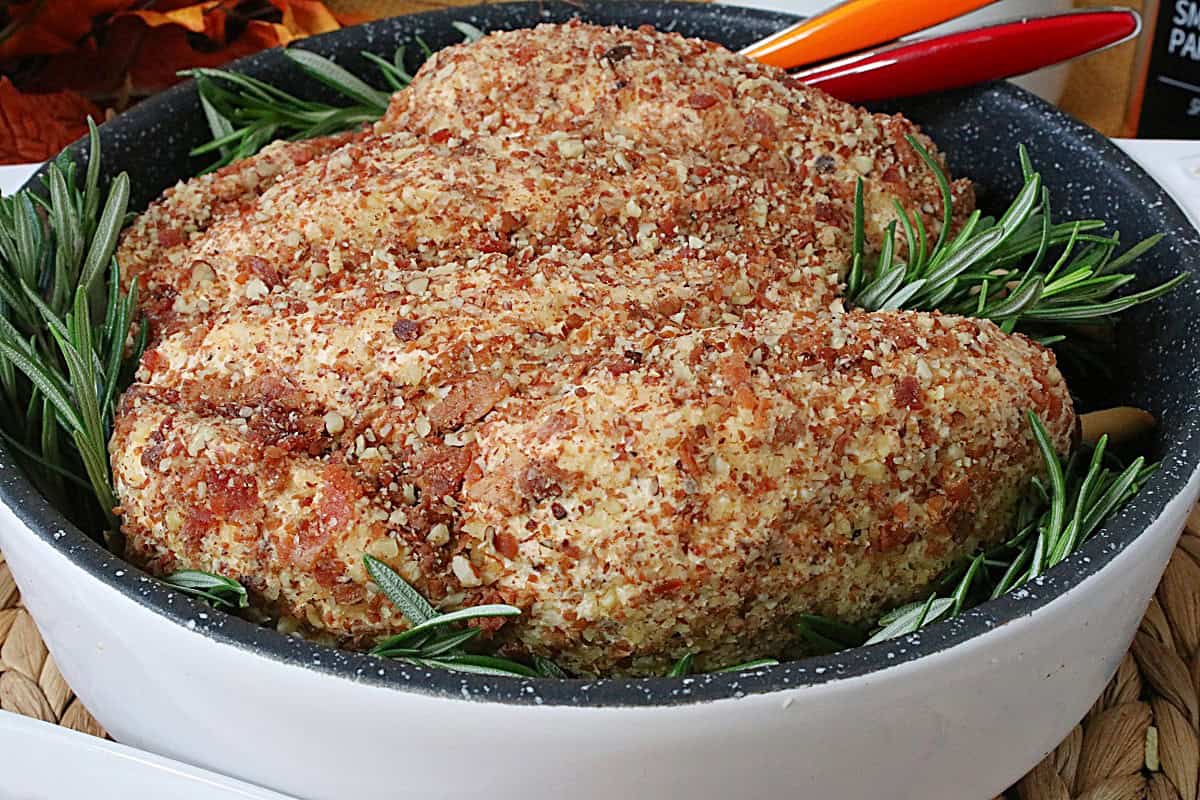 A small white roasting pan with a turkey cheeseball appetizers inside along with some fresh rosemary.