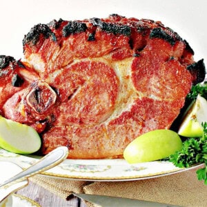 A large bone-in spiced apricot glazed ham on a pretty porcelain platter.