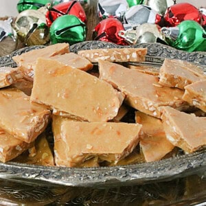 Shards of Almond Butter Crunch Candy in a dish with colorful jingle bells in the background.