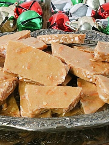 Shards of Almond Butter Crunch Candy in a dish with colorful jingle bells in the background.
