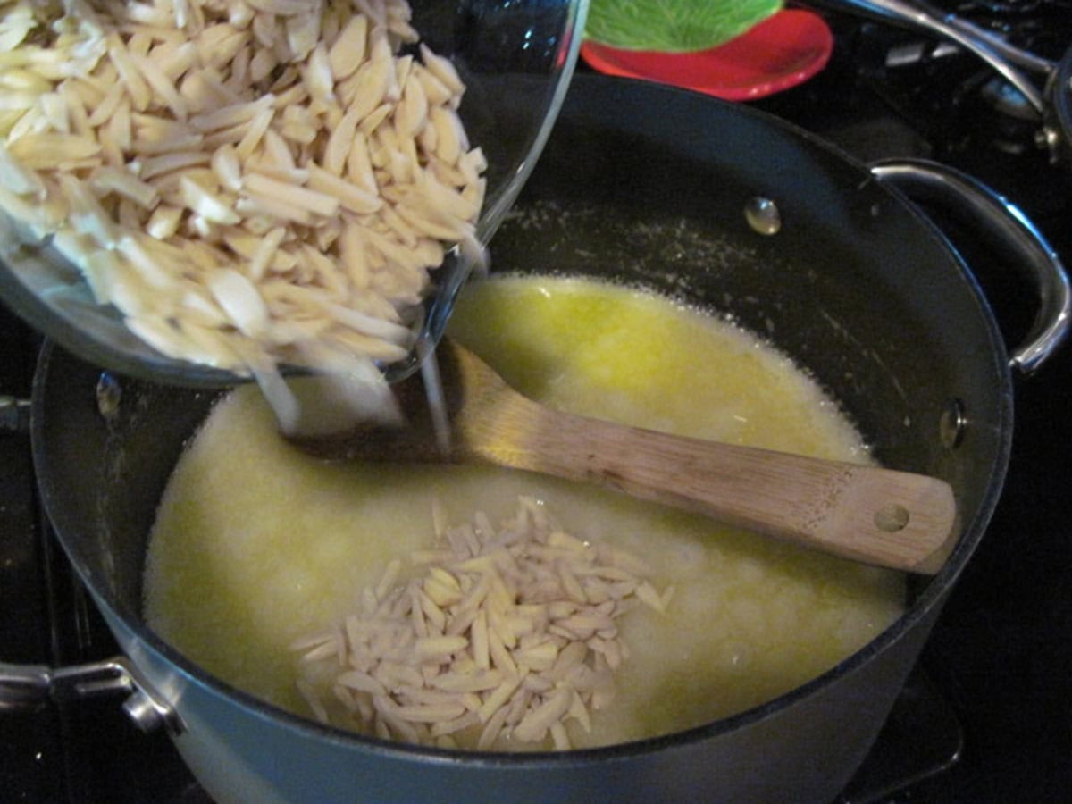 Slivered almonds being added to a saucepan with butter and sugar for making candy.