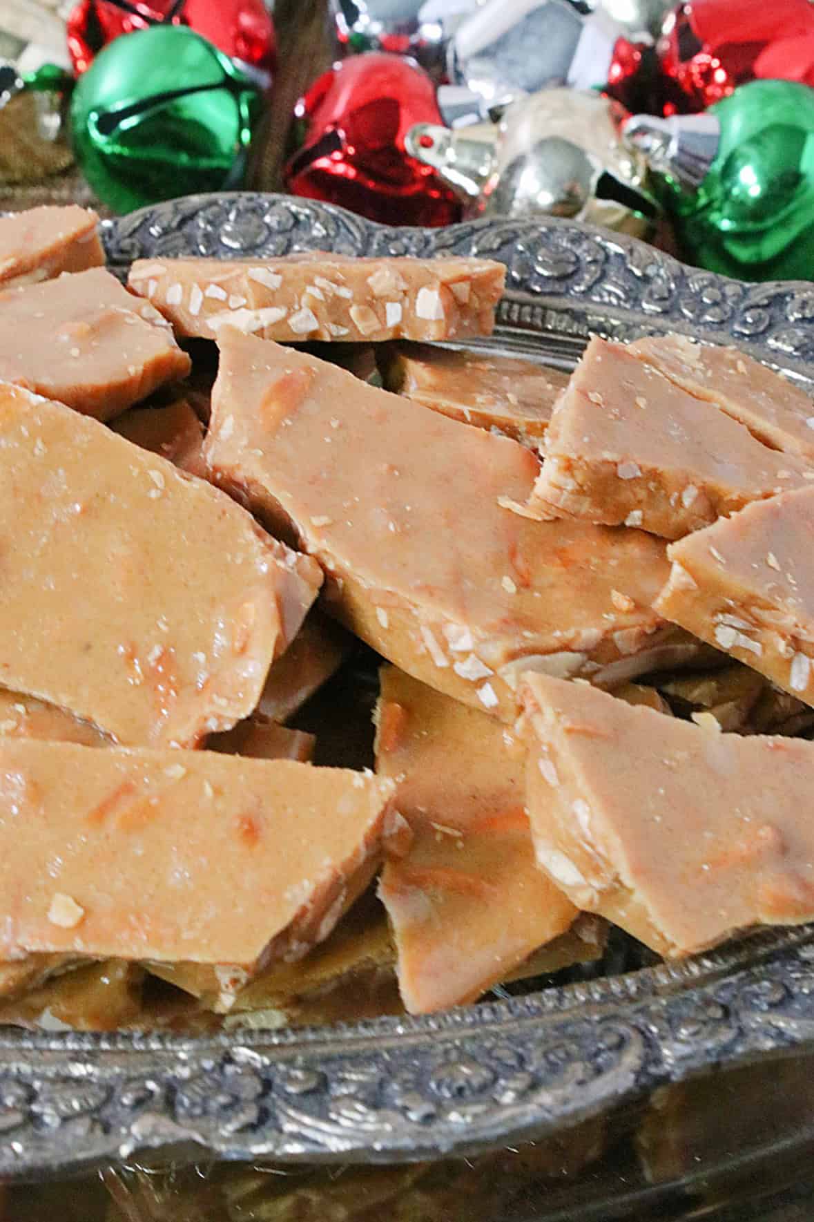 A silver and glass container overflowing with almond butter crunch candy pieces.