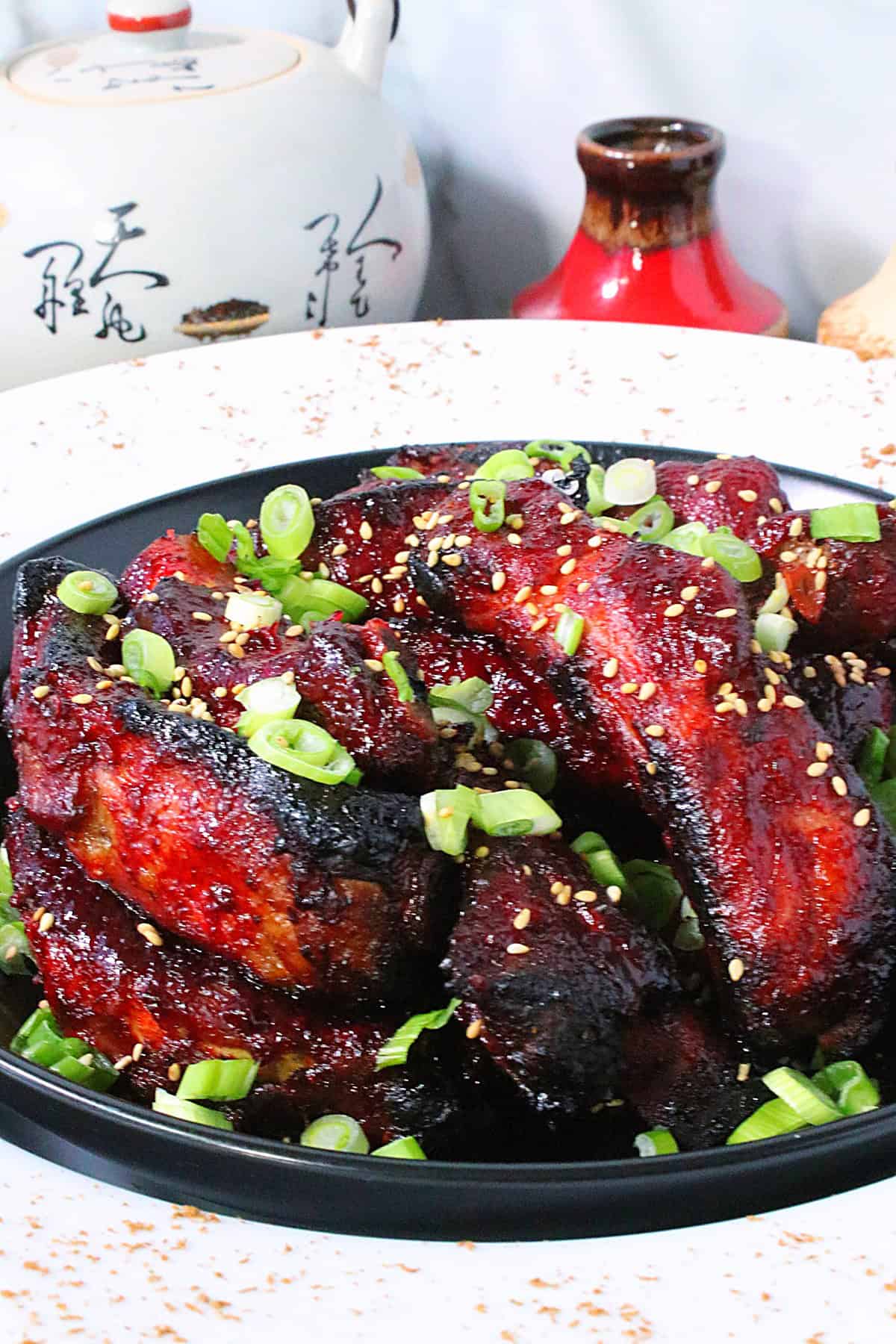 Deliciously caramelized, red Chinese 5-spice ribs in a bowl and topped with sesame seeds and chopped scallions.
