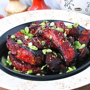 Individual Chinese 5-spice ribs in a black bowl topped with chopped scallions and sesame seeds.
