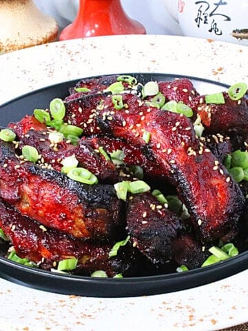 Individual Chinese 5-spice ribs in a black bowl topped with chopped scallions and sesame seeds.