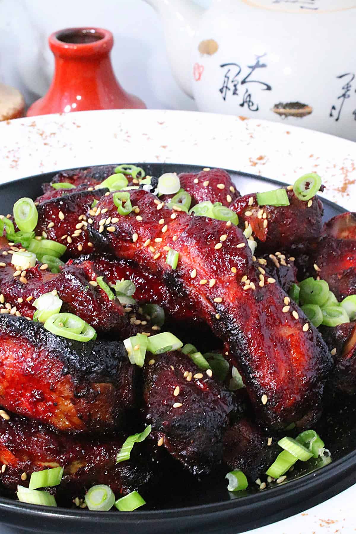 An Asian themed photo of Chinese 5-spice sticky ribs in a black bowl with a a Chinese tea pot in the background.