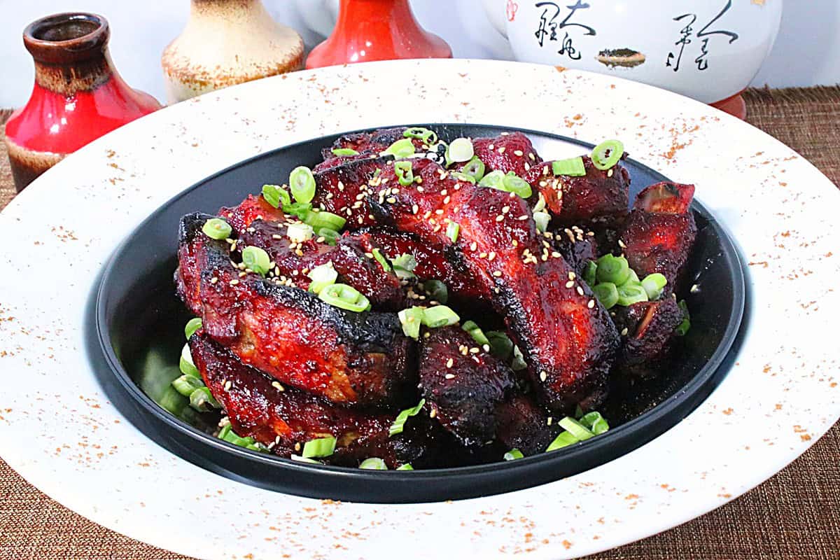 A completed dish of Chinese 5-spice sticky ribs in a white and black bowl sprinkled with 5 spice powder on the edges.
