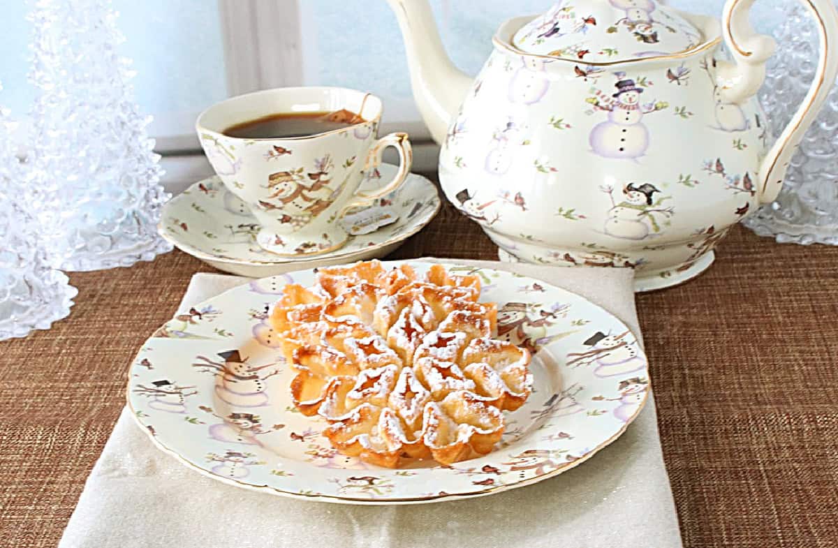 A cozy setting with a winter scene and a fried rosette cookie on a snowman plate.