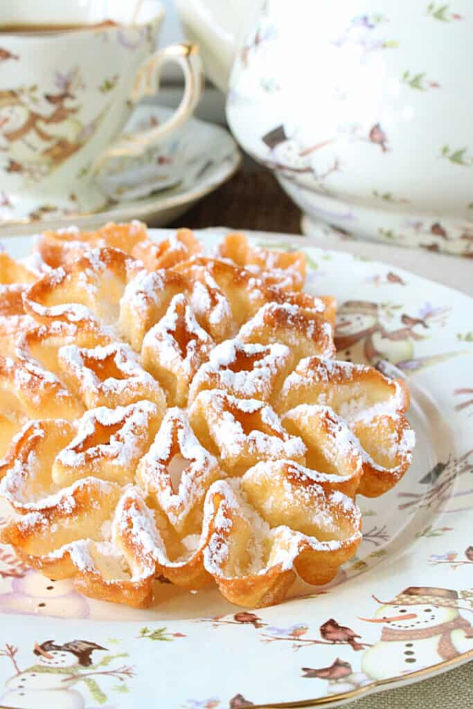 A delicious looking crispy brown, fried rosette snowflake cookie dusted with confectioner's sugar.