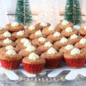A bunch of festive vintage holiday nut cup cookies in mini red cupcake liners on a glass plate with fairy lights in the background.