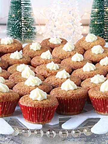A bunch of festive vintage holiday nut cup cookies in mini red cupcake liners on a glass plate with fairy lights in the background.