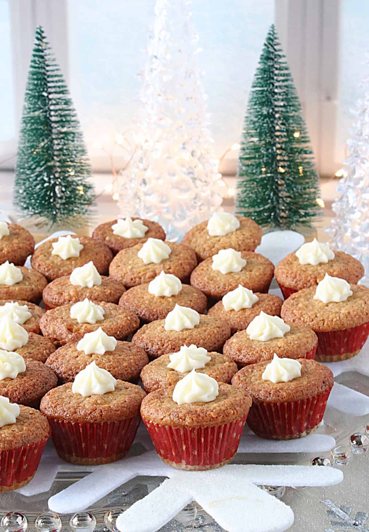 Mini muffin tin holiday nut cup cookies on a glass platter with cute bottle tree Christmas trees in the background.