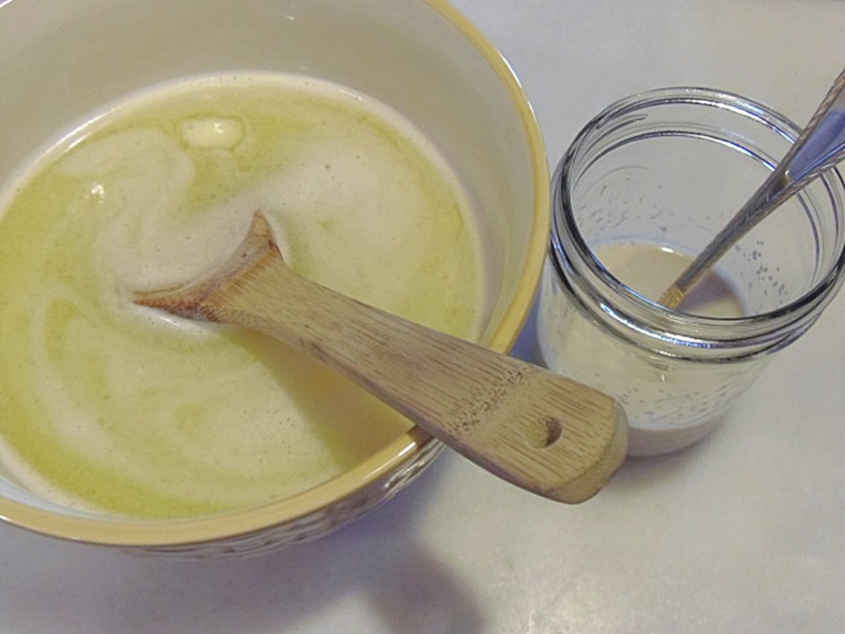 A bowl with melted butter, water, and a wooden spoon next to a jar with a yeast mixture.
