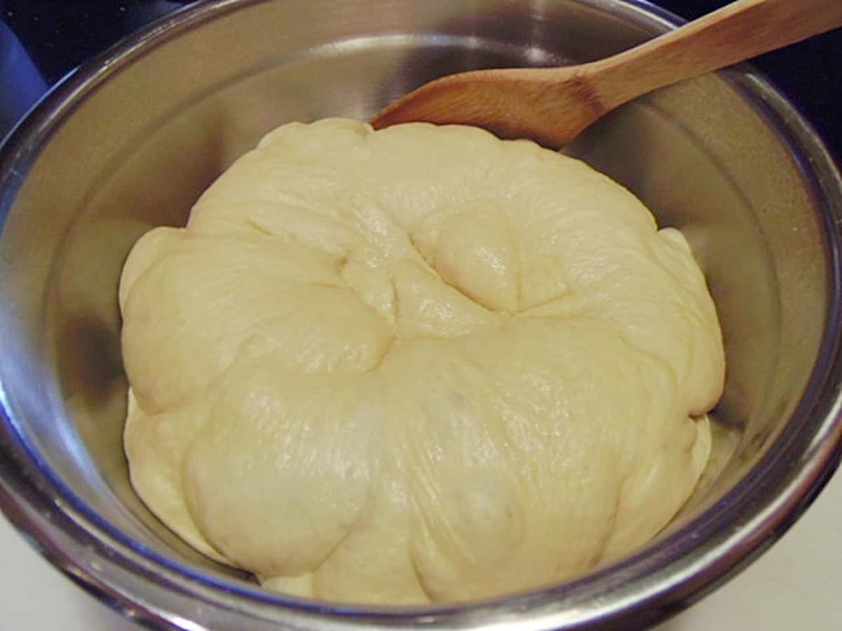 A silver bowl filled with proofed cinnamon roll dough.