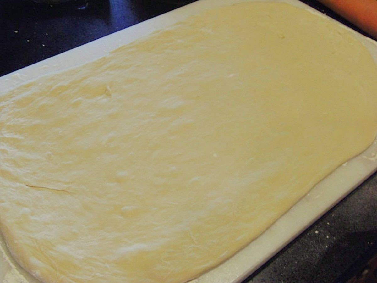 A rectangle of unbaked cinnamon roll dough on a floured surface.