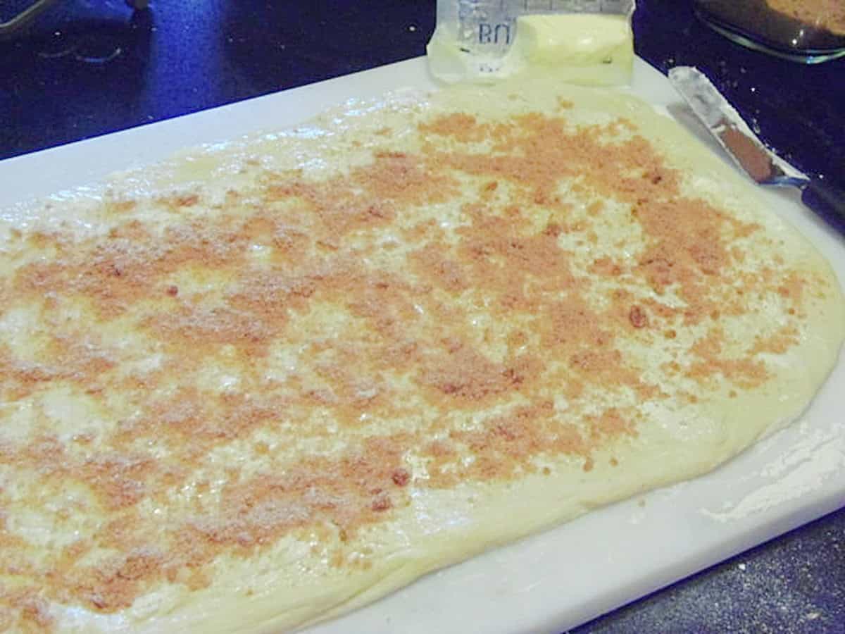 A rectangle of dough topped with butter and cinnamon sugar.