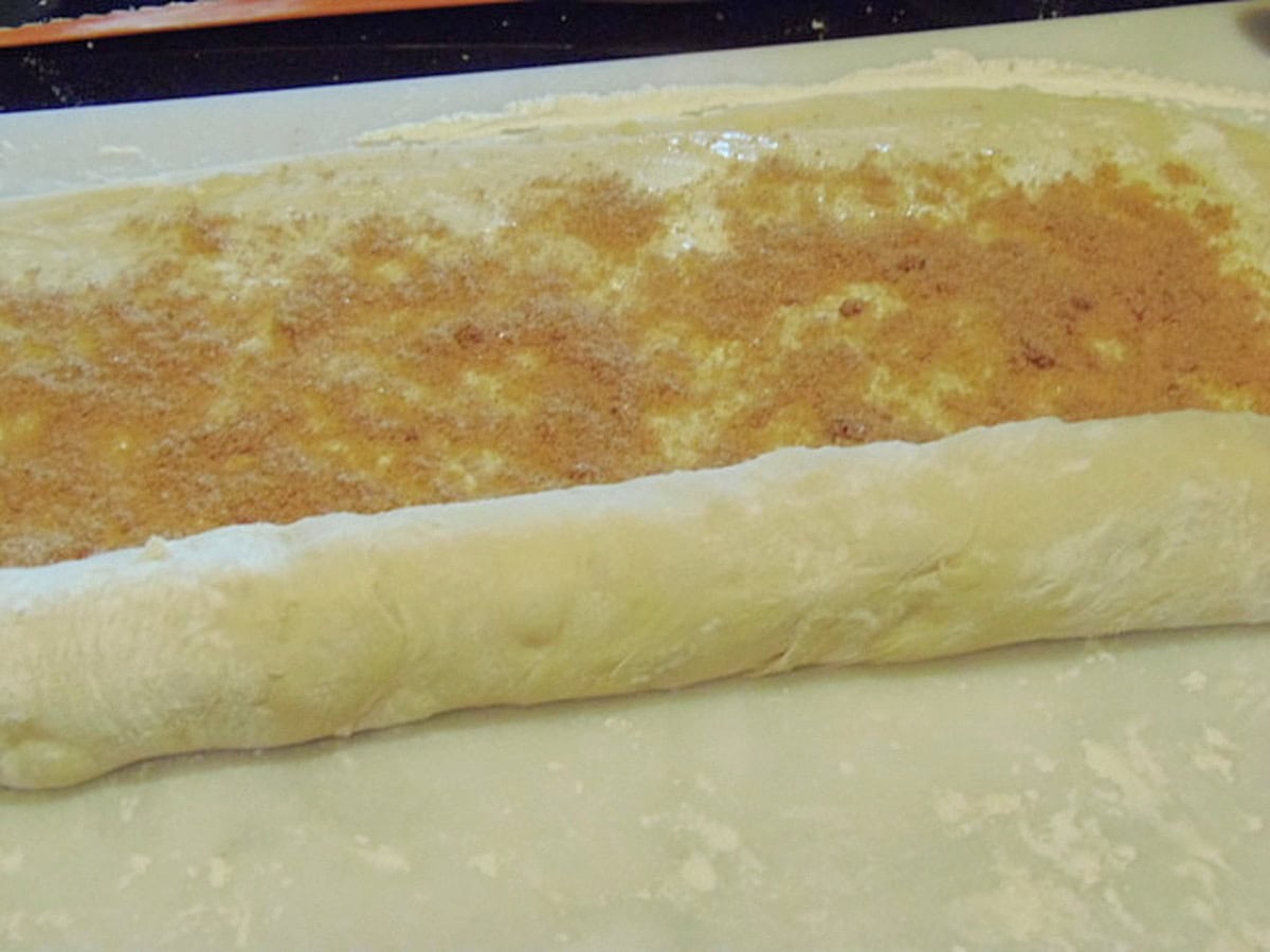 Cinnamon and sugar being rolled into dough for making cinnamon rolls.