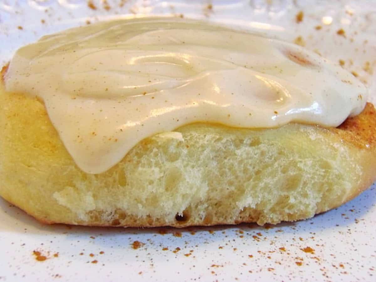A beautifully golden cinnamon roll on a plate with icing and cinnamon.