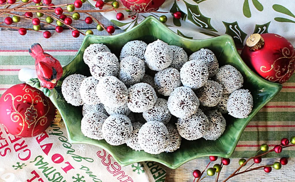 A bunch of holiday nonpareil chocolate peppermint truffles in a green holly berry shaped bowl.