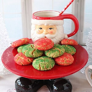 A Santa cake stand with feet holding a bunch of red and green Christmas cookies.