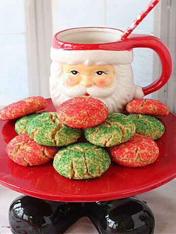 A Santa cake stand with feet holding a bunch of red and green Christmas cookies.