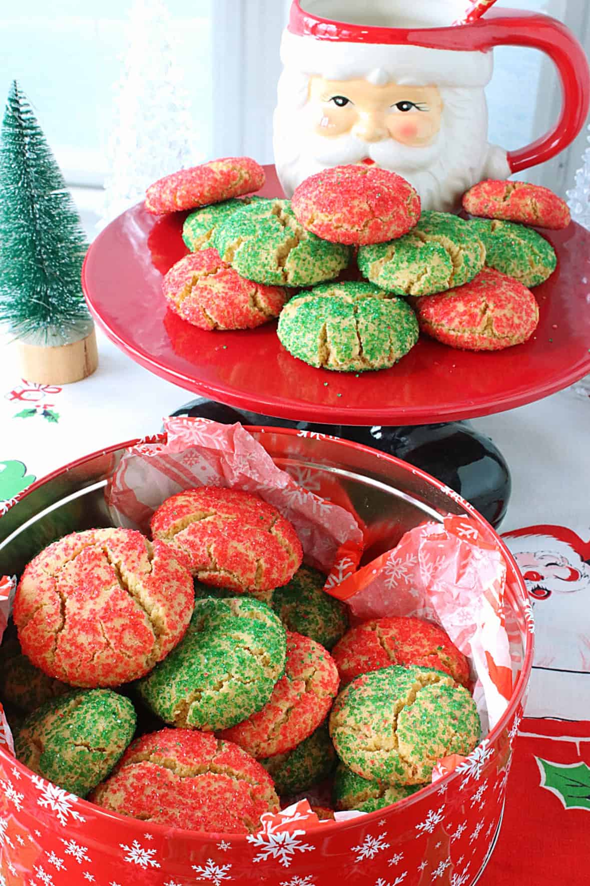 I've been making Santa's Favorite Sugar Cookies every year since I was newly married (36 years ago). And before that, it was my favorite Christmas cookie as a child. It's the cookie that brings back the most wonderful holiday memories for our sons and me, and it's the cookie that we all still consider one of our very favorite Christmas food traditions. - Kudos Kitchen by Renee A Christmas cake plate and cookie tin filled with red and green sugar cookies for Christmas.