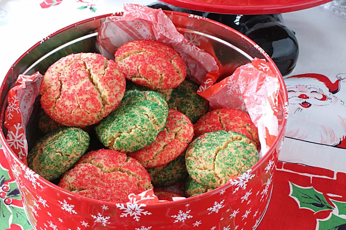 I've been making Santa's Favorite Sugar Cookies every year since I was newly married (36 years ago). And before that, it was my favorite Christmas cookie as a child. It's the cookie that brings back the most wonderful holiday memories for our sons and me, and it's the cookie that we all still consider one of our very favorite Christmas food traditions. - Kudos Kitchen by Renee A red cookie tin with tissue paper filled with red and green Christmas cookies.