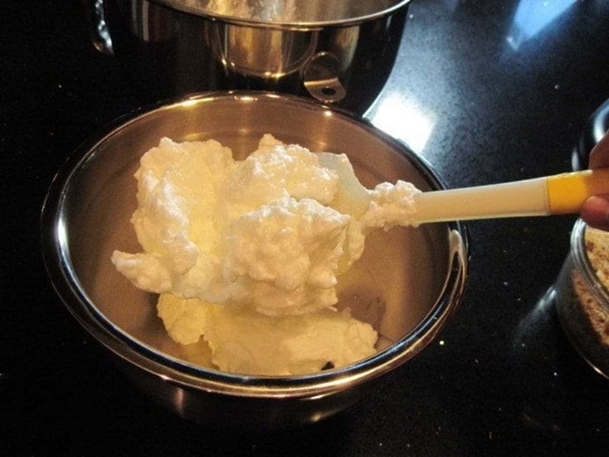 Fluffy beaten egg whites in a silver bowl with a spatula.