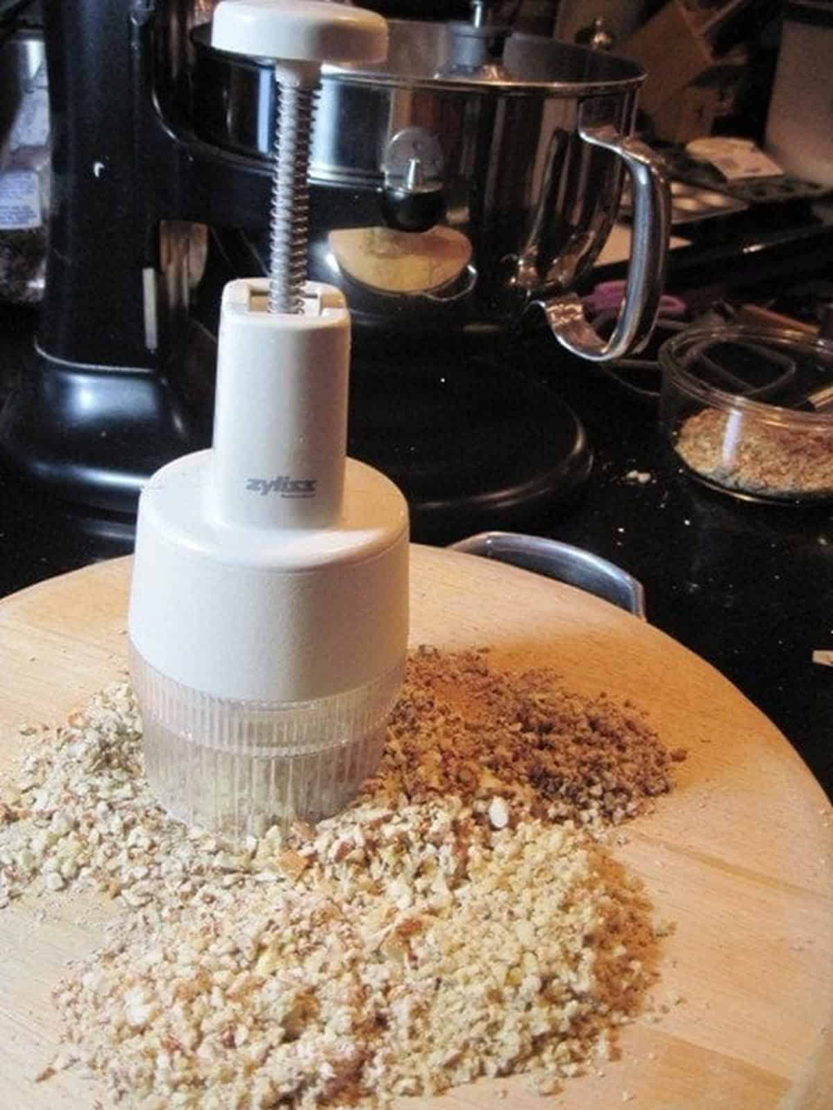 Finely chopped nuts on a wooden cutting board with a nut chopper on the side.
