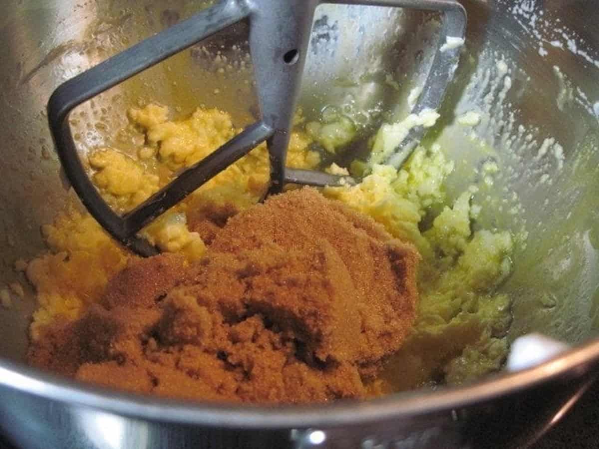 A stand mixer bowl with the paddle attachment along with brown sugar and butter in the bowl.