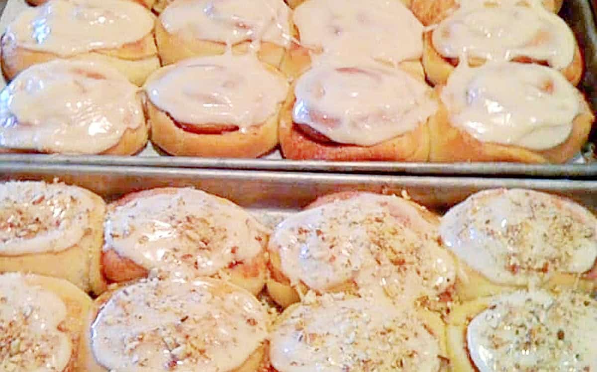 Two baking sheets filled with mashed potato cinnamon rolls. Some have chopped pecans on top and some are plain.