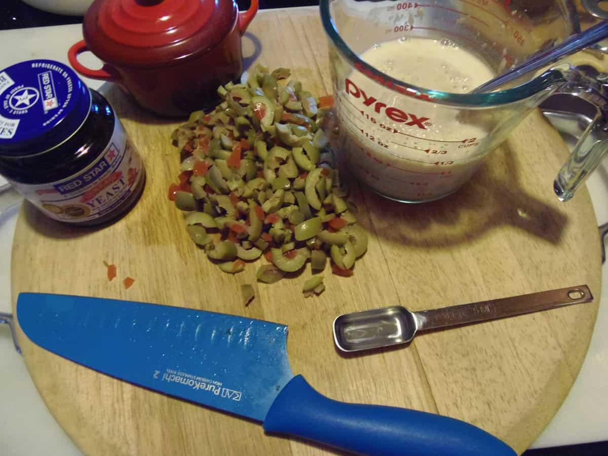 The ingredients for making olive bread on a wooden cutting board.