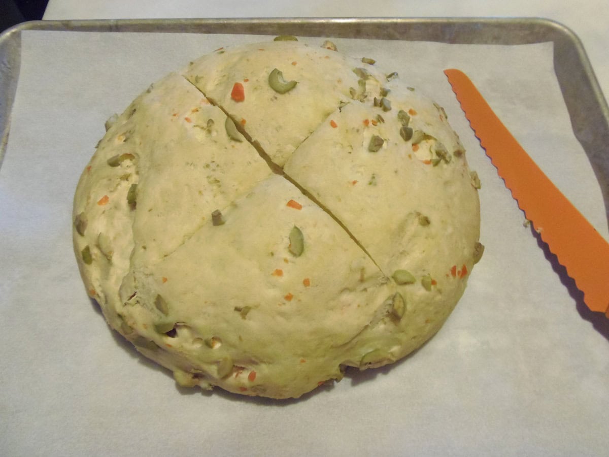 Un unbaked loaf of rustic olive bread with an X sliced into the top.