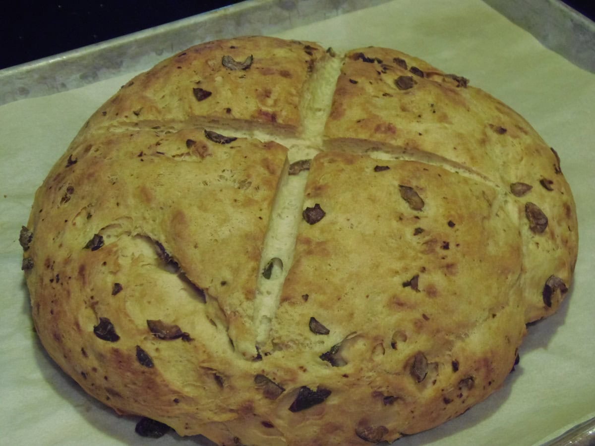 A baked rustic olive bread on a parchment lined baking sheet.
