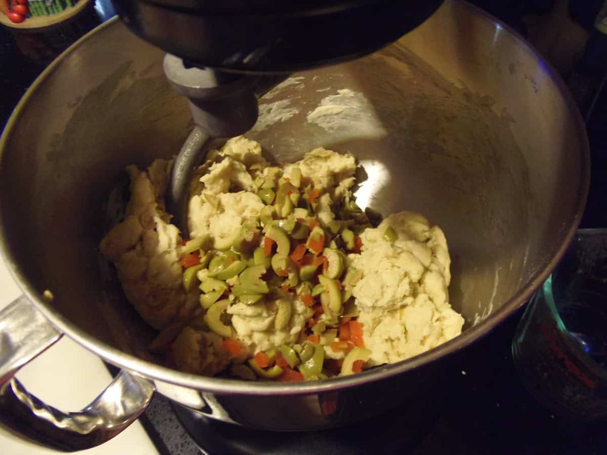 Chopped olives added to the bowl of a stand mixer for making olive bread.